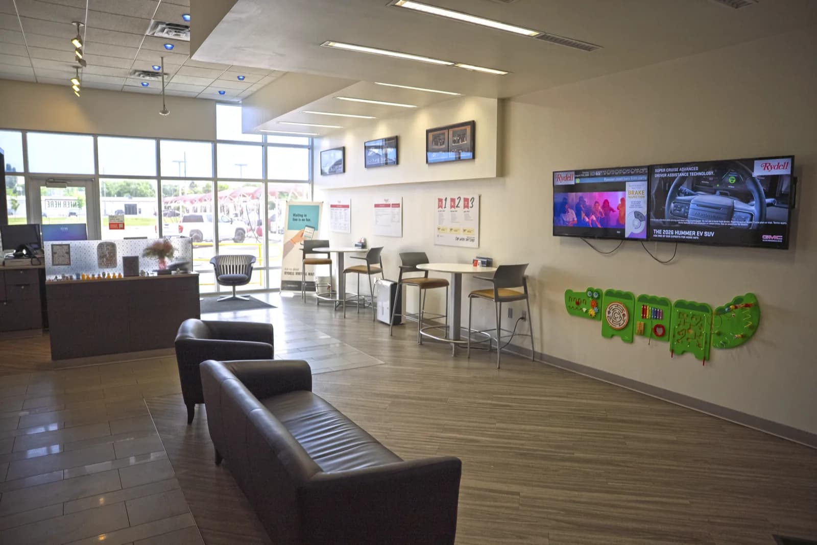 The customer lounge at the Rydell Detail Center: leather seating and high-top tables facing wall-mounted TVs, with the service desk and street-facing windows beyond.