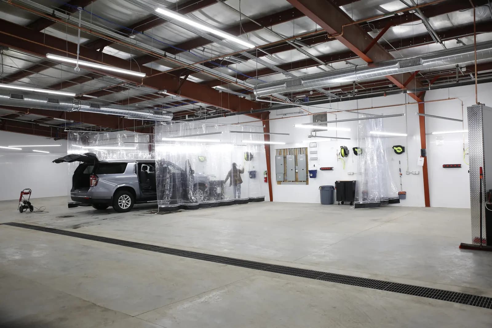 The Rydell detail shop: a vehicle in an enclosed bay with its hatch open, curtained work stalls, and floor drains running the length of the building.