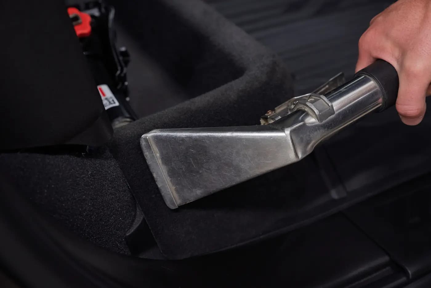 A detailer shampooing a vehicle's carpet with an upholstery extractor.